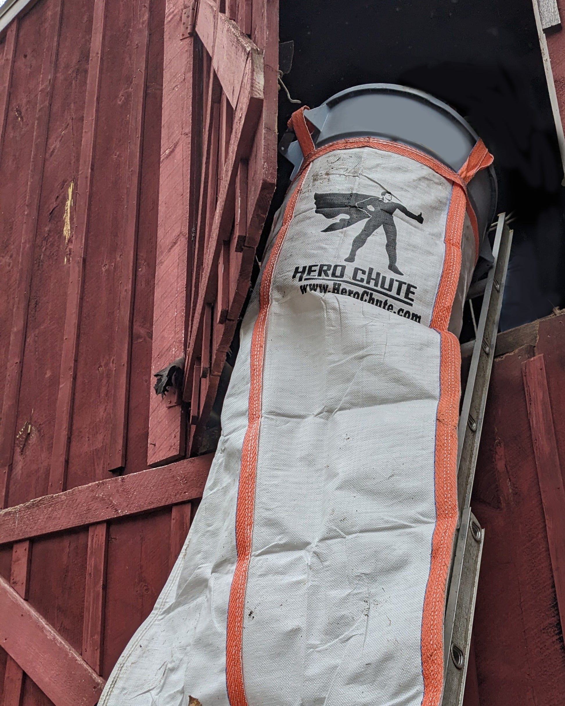 A Hero Chute heavy duty construction chute section leaning against a wooden barn wall, used in construction site cleanup.